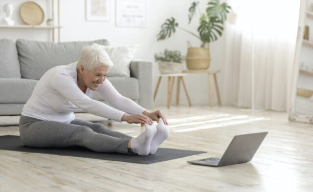 Middle-aged woman stretching in front of a laptop